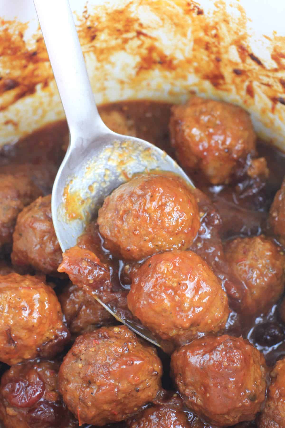 large metal spoon with 2 meatballs out of the crockpot