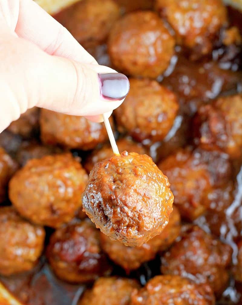 hand lifting a meatball out of the crockpot on a toothpick