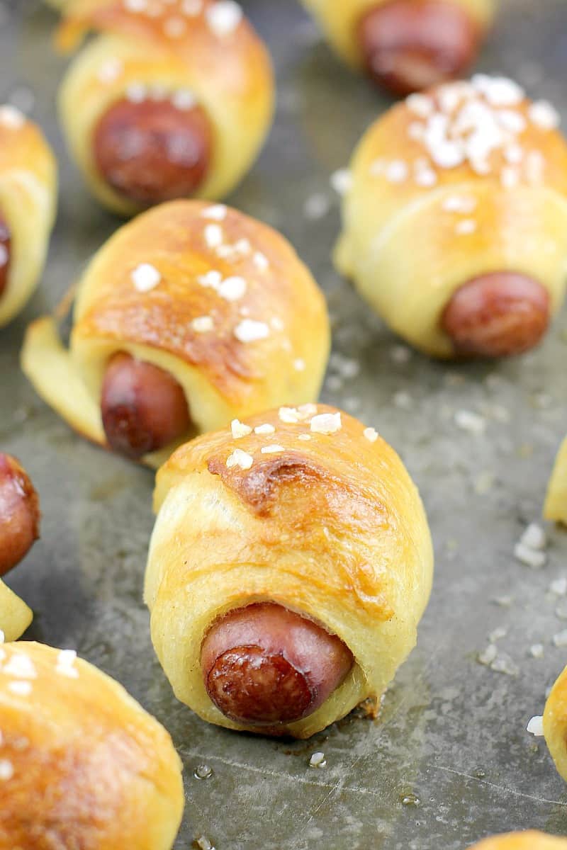 angled view of cooked mini pretzel pigs on a grey bake sheet sprinkled with salt