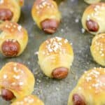 zoomed out view of cooked mini pigs in a blanket on a bake sheet sprinkled with salt