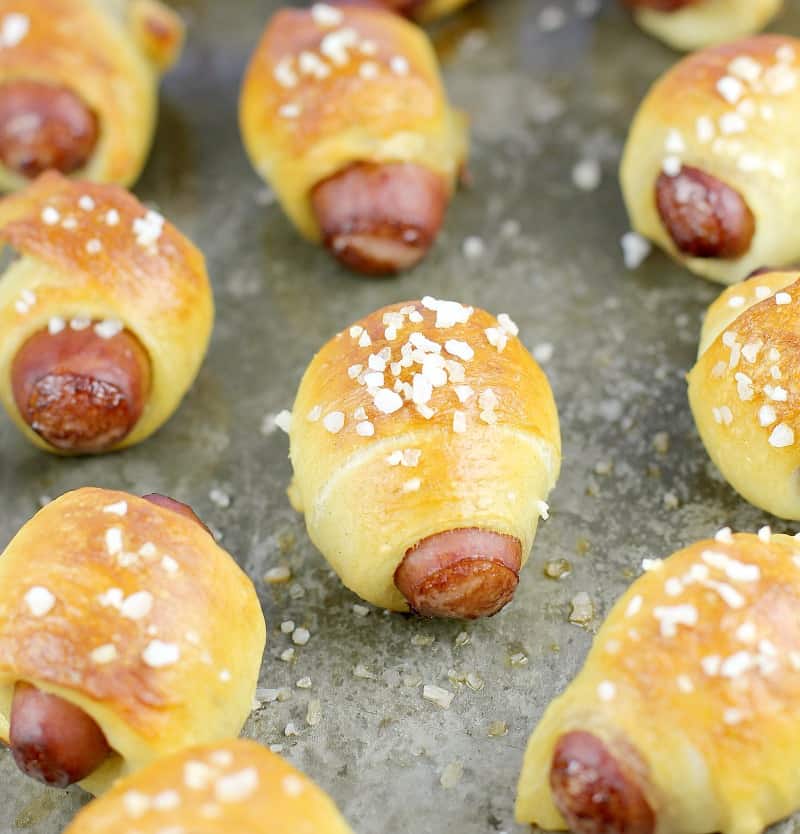 zoomed out view of cooked mini pigs in a blanket on a bake sheet sprinkled with salt