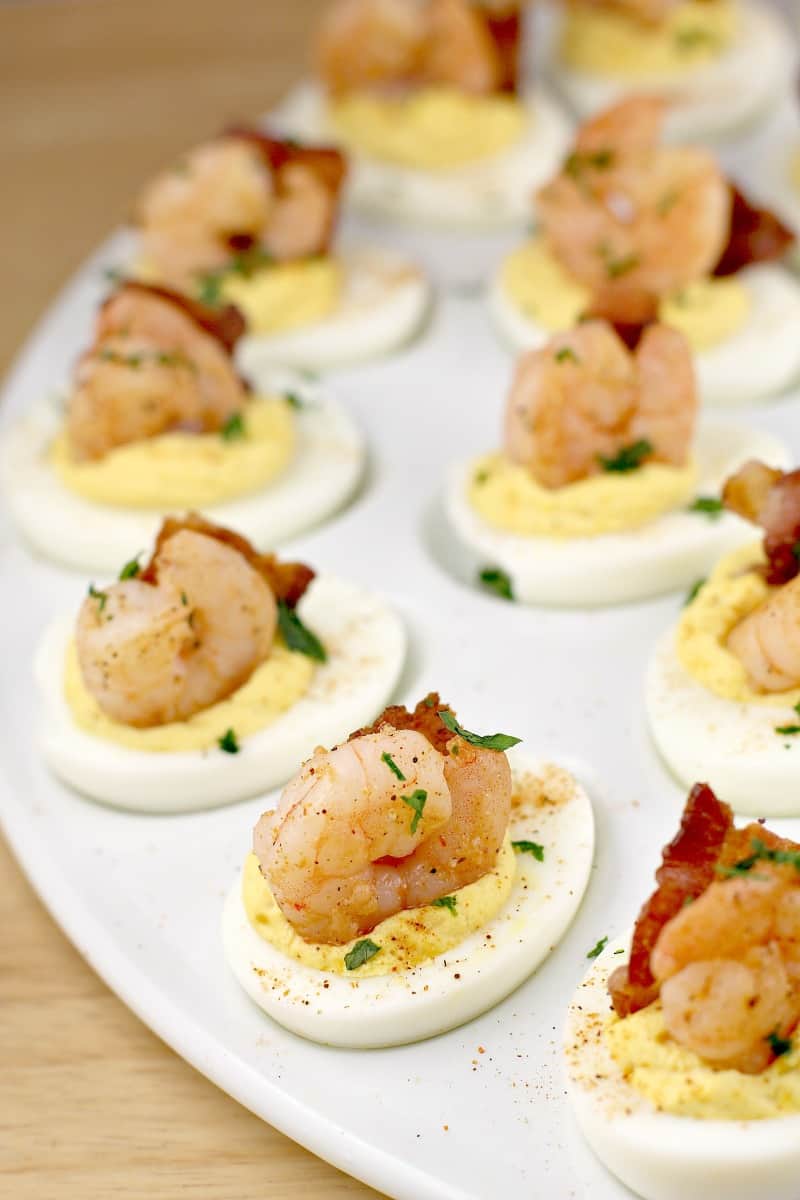 creole shrimp recipe on deviled eggs with bacon on a white platter; parsley sprinkled overtop