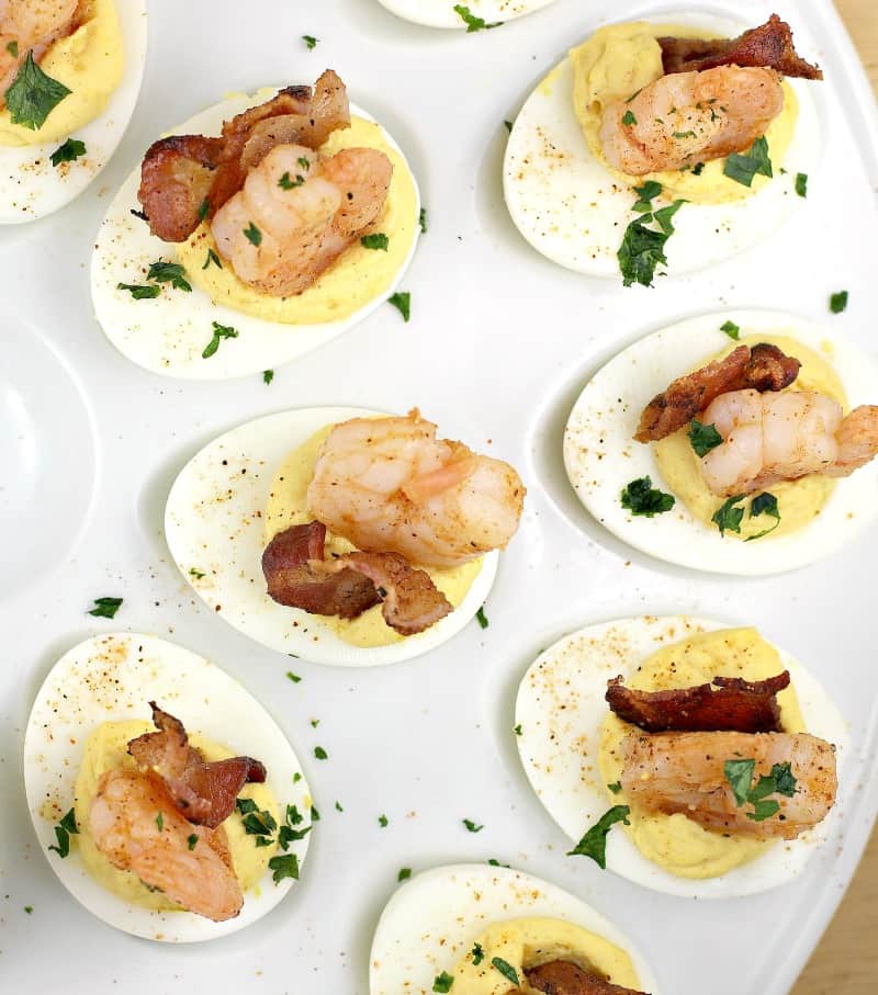 top down view of deviled eggs recipe finished on a white platter with shrimp and bacon on top, garnished with parsley