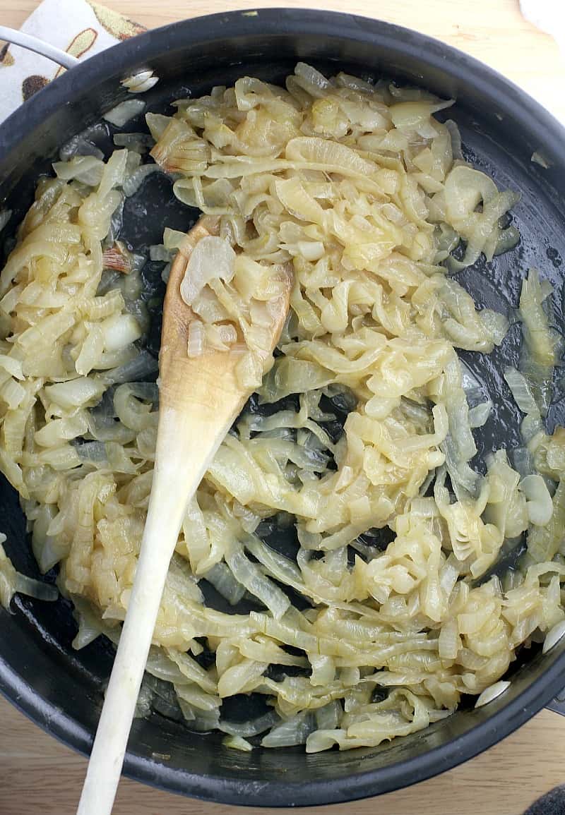 the finished caramelized onions in a black skillet with wooden spoon