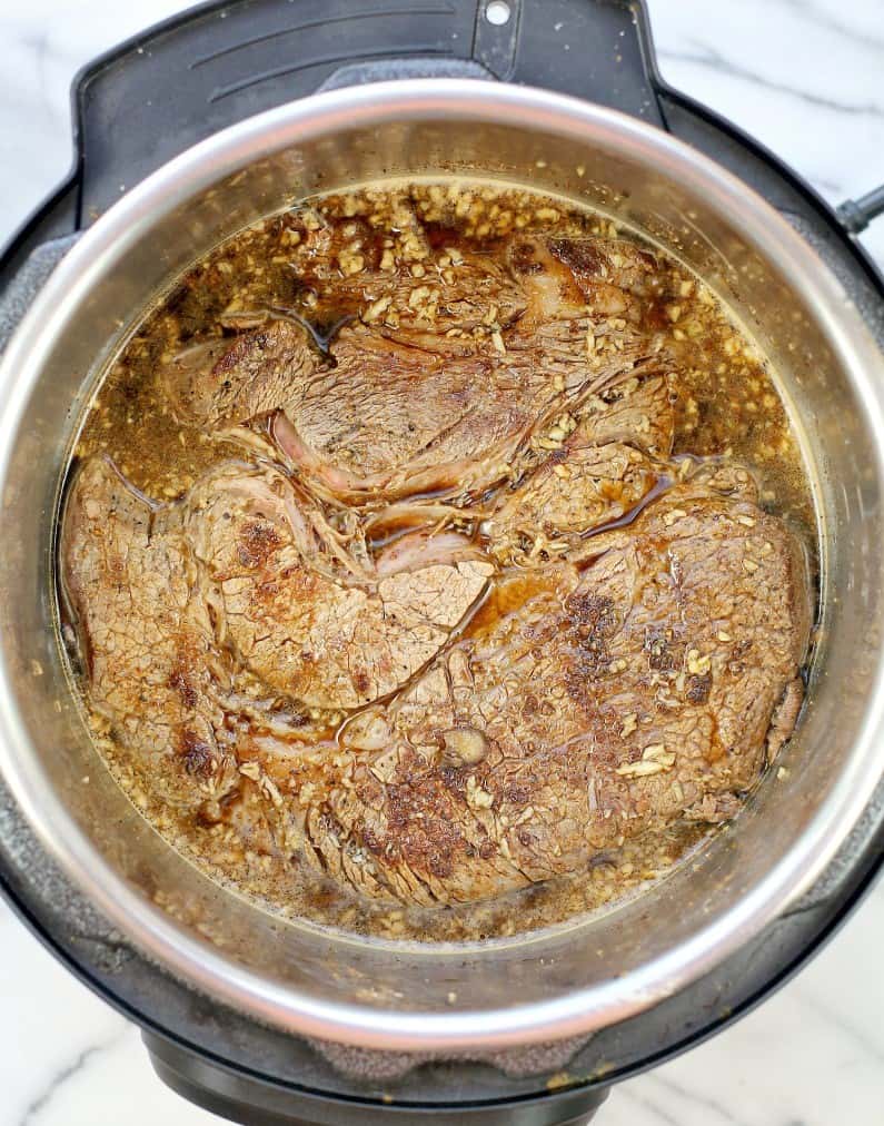 top down view of the instant pot pot roast seared, in the bear-garlic mixture, before adding the remaining ingredients