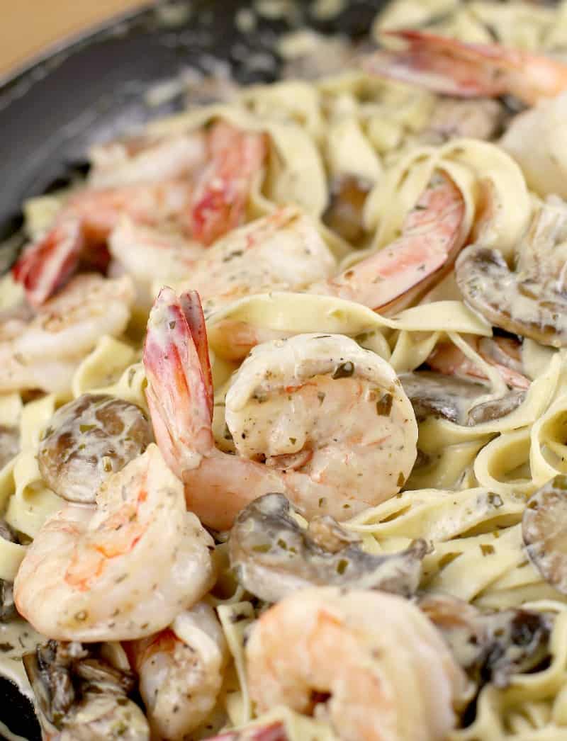 close in view of the shrimp and mushrooms added to the pasta with the pesto sauce in a skillet