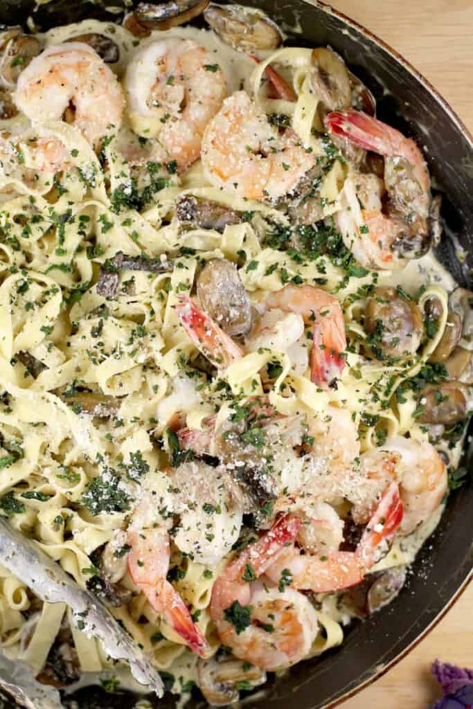 top down view of the shrimp and pasta in a large skillet garnished with basil and parmesan, in a skillet with thongs in the corner