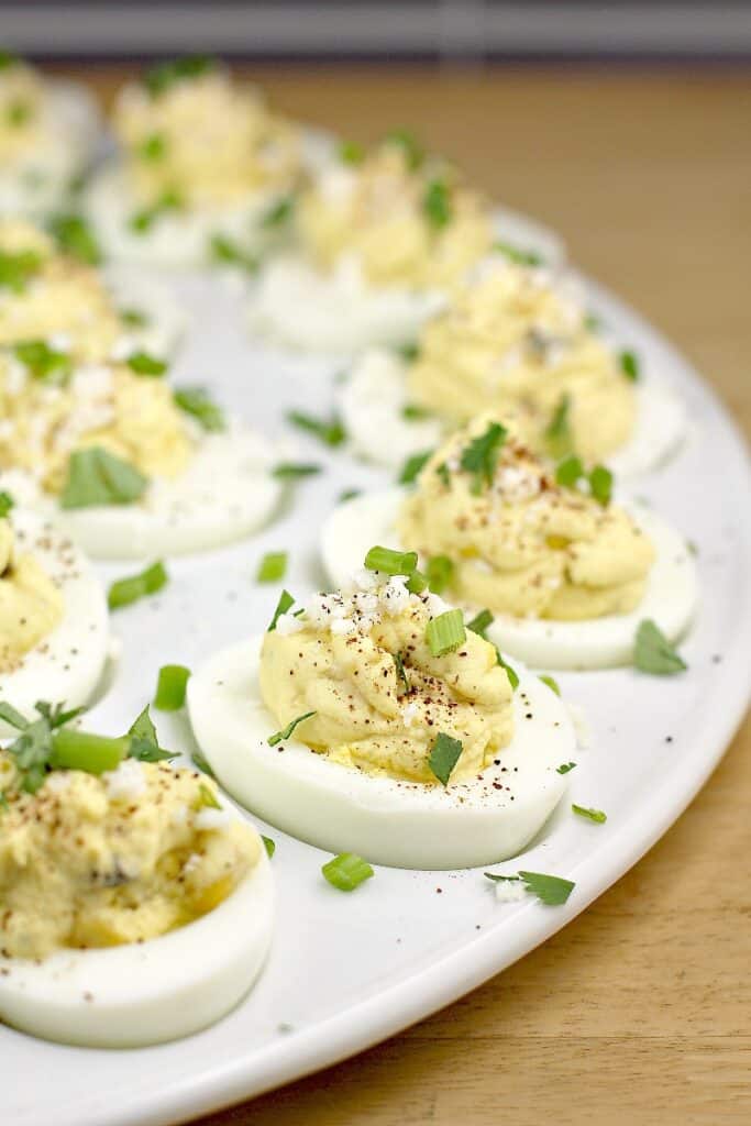 deviled eggs on a white serving platter with green herbs sprinkled over