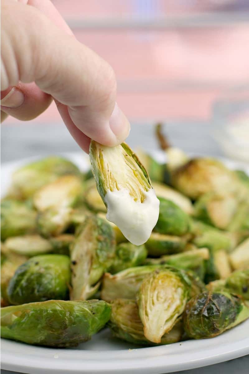 hand holding a brussel sprout coated with lemon aioli