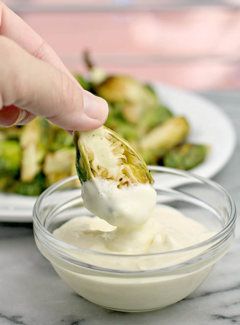 hand holding brussel sprout dipping in a small glass bowl of lemon aioli