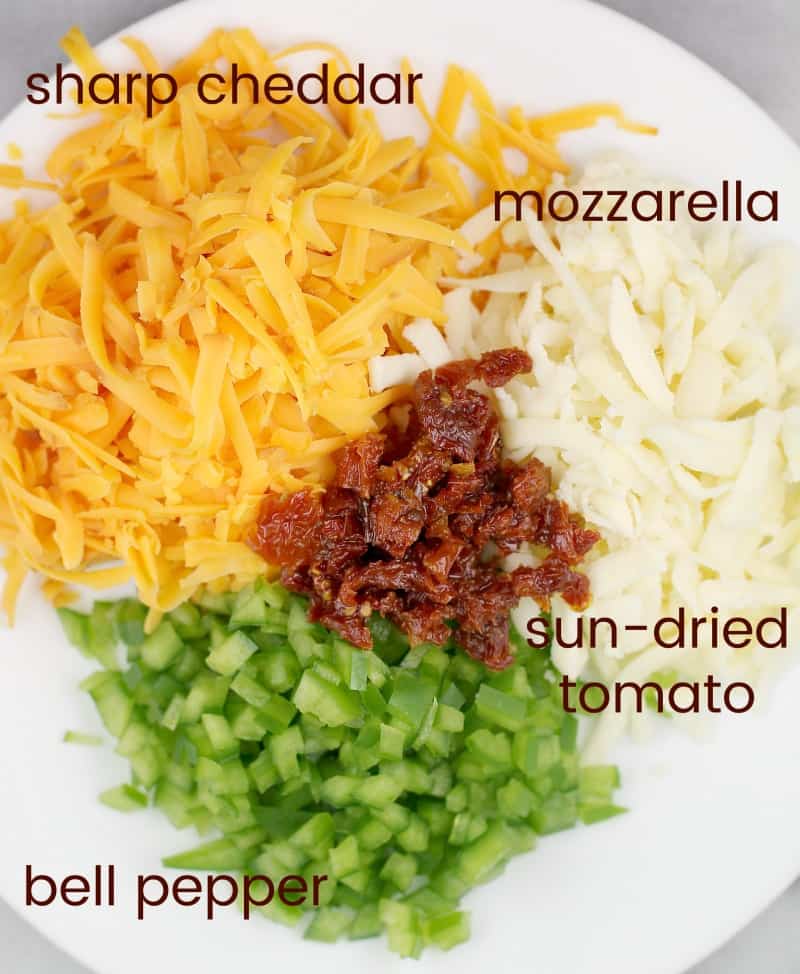 view of the ingredients in a bowl: cheddar, mozzarella, sun-dried tomato, and green bell pepper
