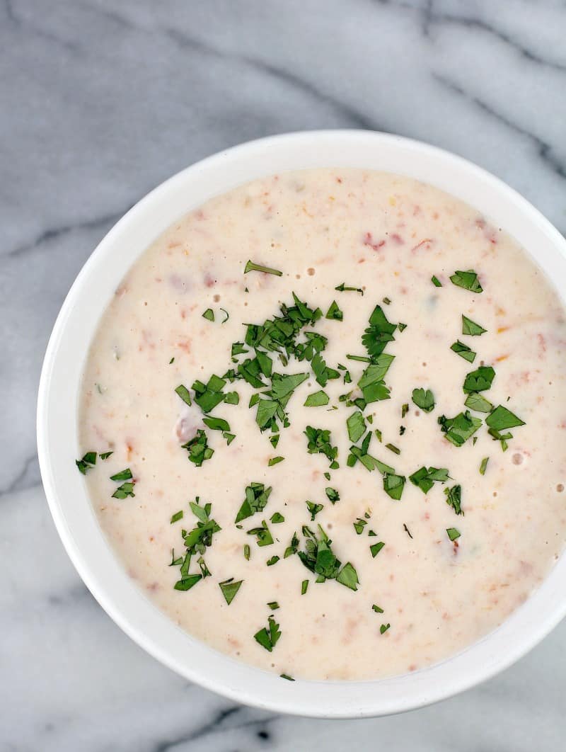 top down view of a bowl full of white queso dip, cilantro scatter on top, bowl is on a marble surface