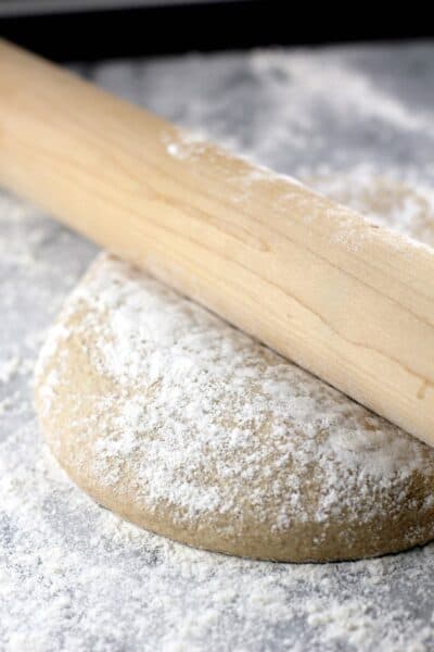 whole wheat pizza dough on a marble surface with a rolling pin