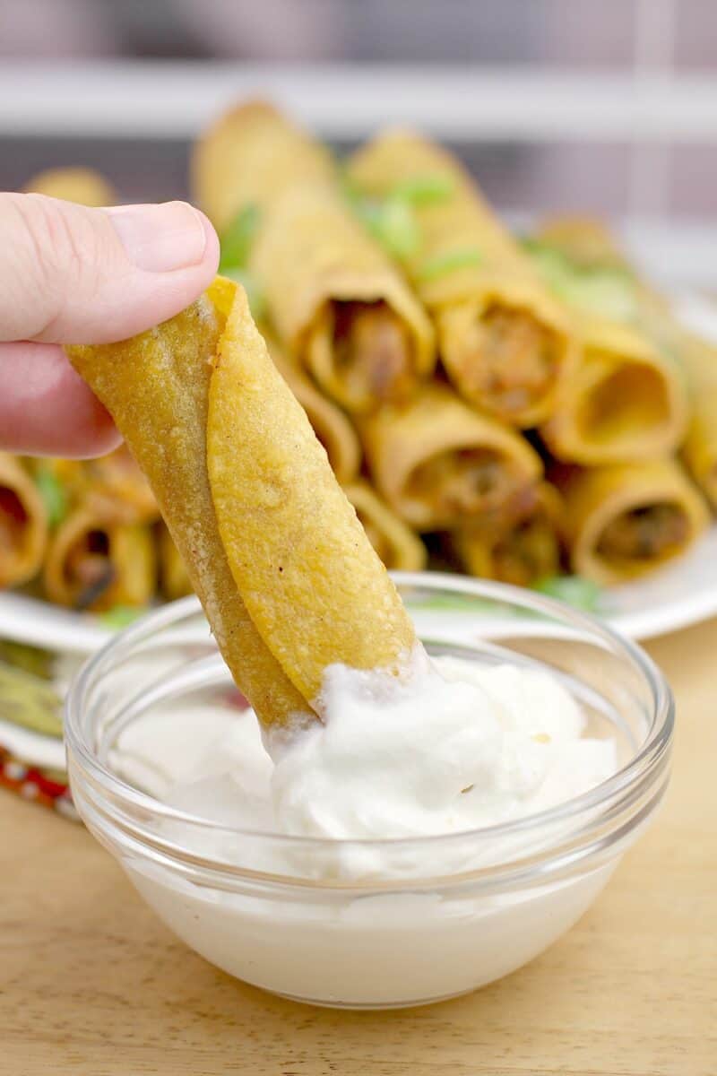 hand dipping taquito in sour cream