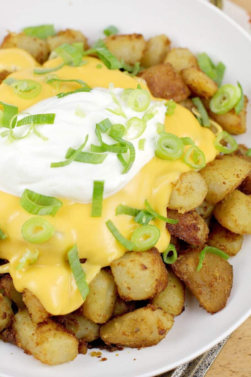 prepared potatoes in a white bowl topped with nacho sauce, sour cream, and green onion