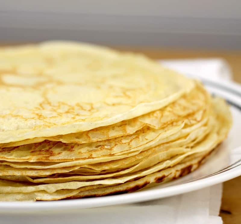 thin crepes in a pile on a white dish, white background