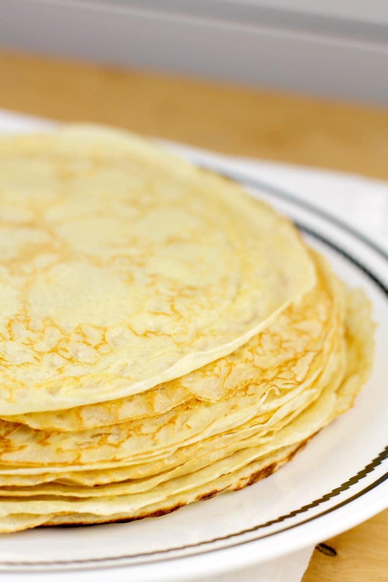 round savory crepes in a stock on a white rimmed dish