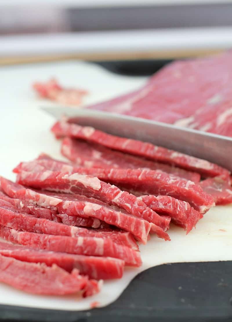 knife slicing flank steak on white board