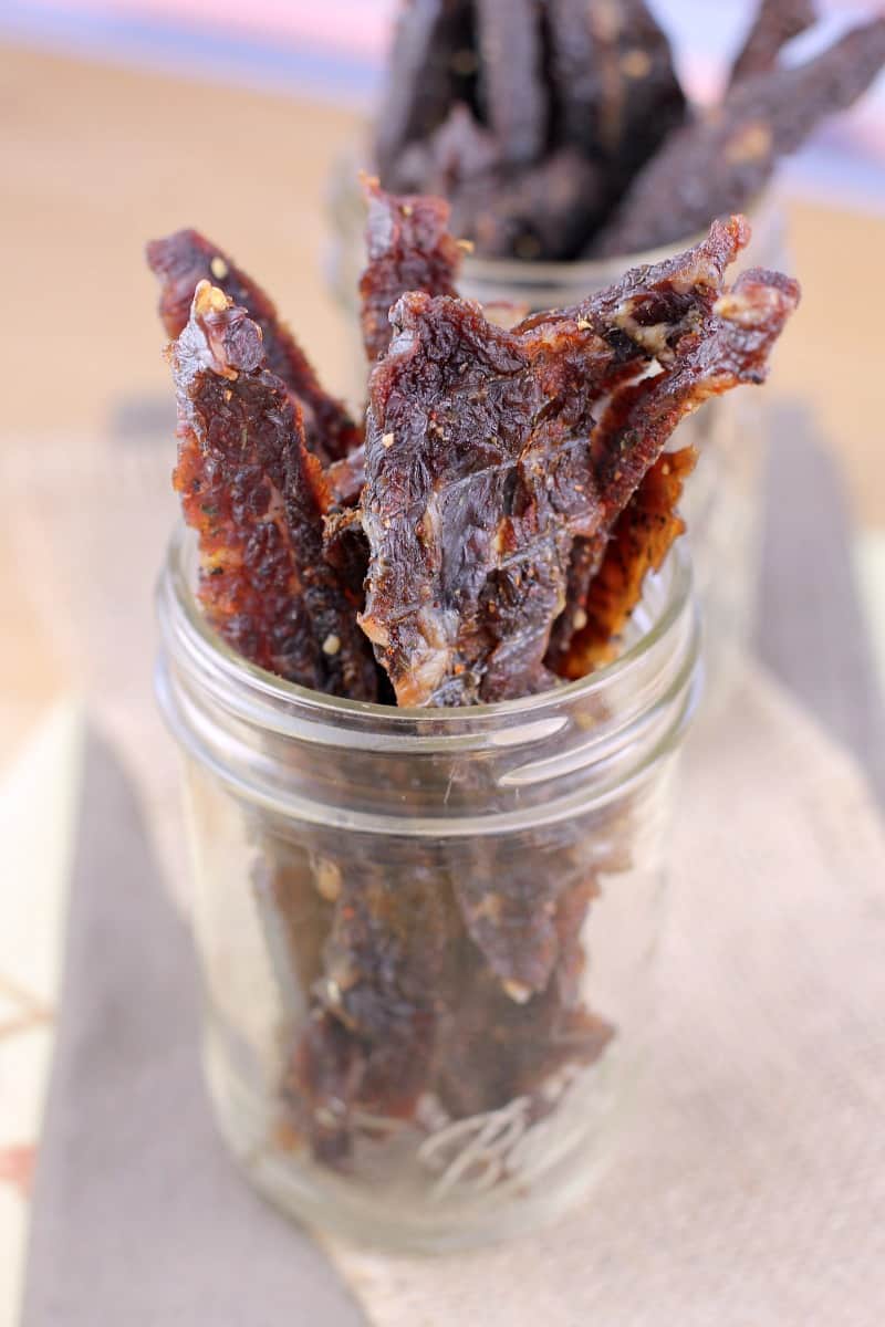 beer bbq beef jerky in a clear mason jar; jar with teriyaki beef jerky in the background