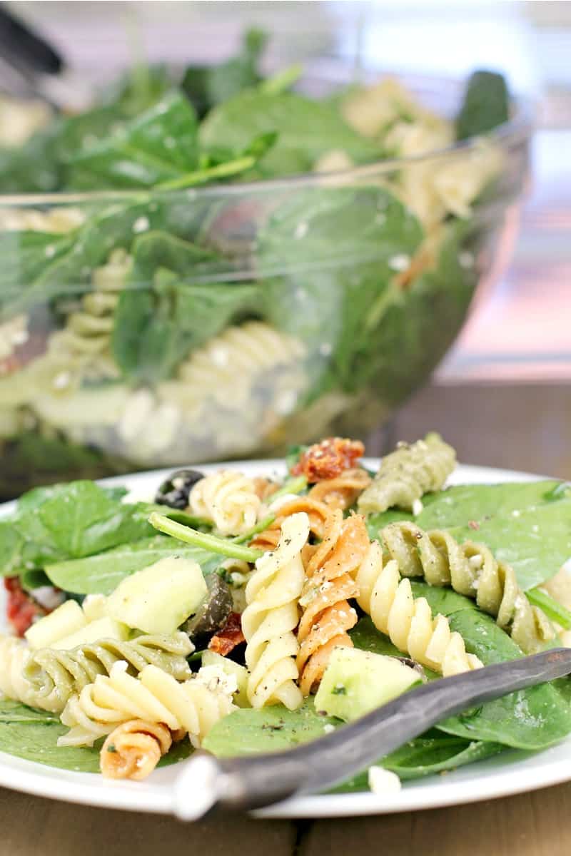 rotini pasta salad on spinach, plated on white plate, salad bowl in the background