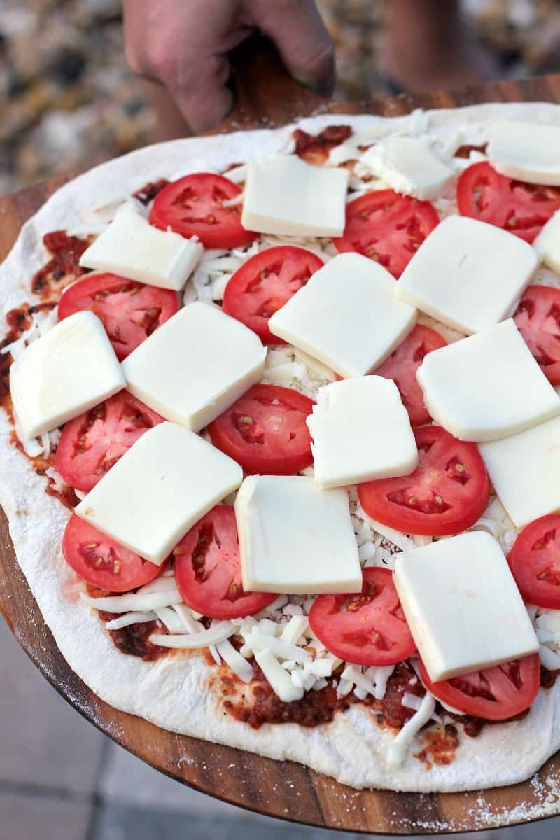 assembled pizza ready to cook topped with slices of tomato and cheese