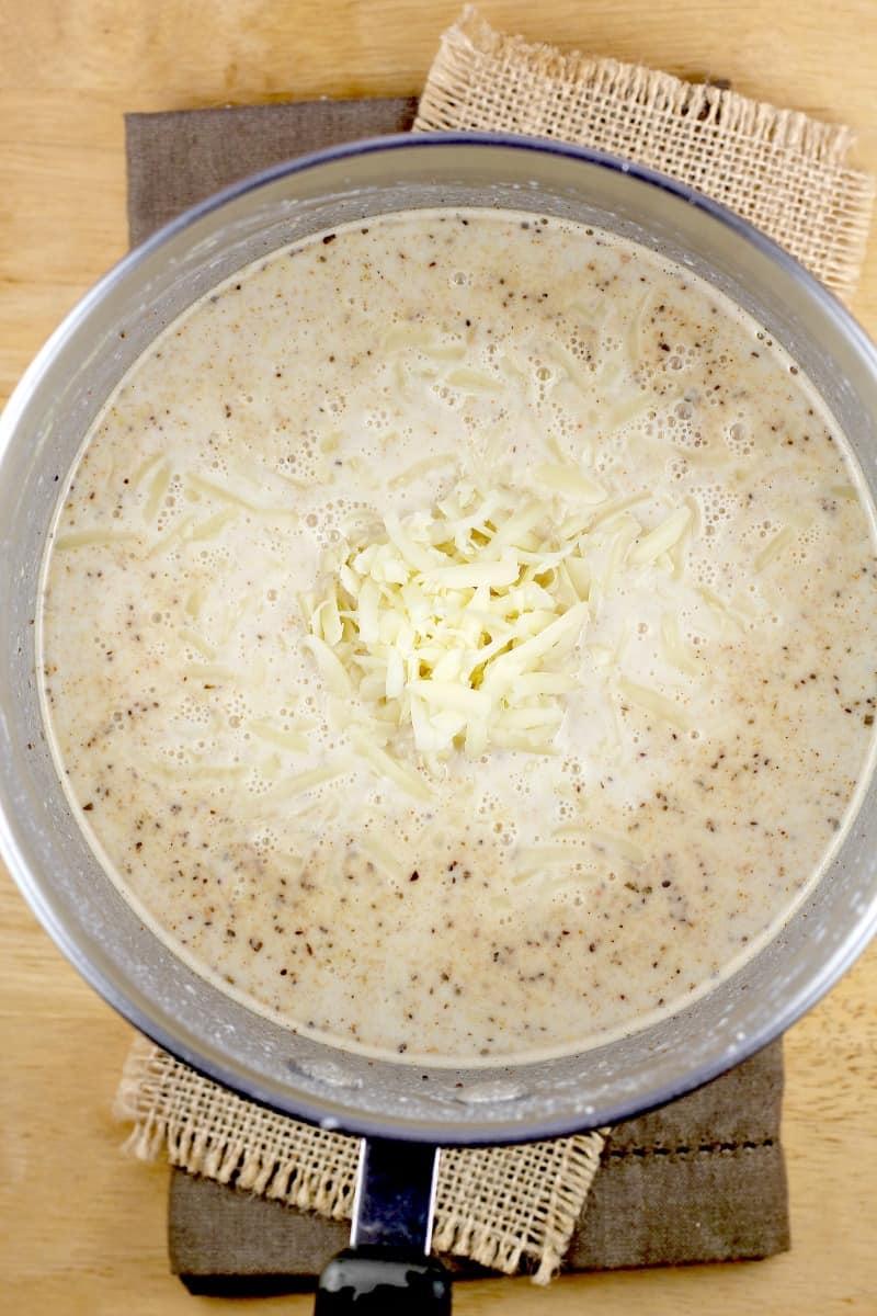 bechamel sauce in a saucepan with shredded cheese added in the center