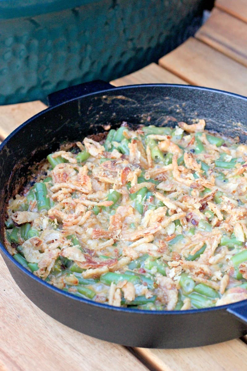 cooked green bean casserole in cast iron skillet on table next to big green egg