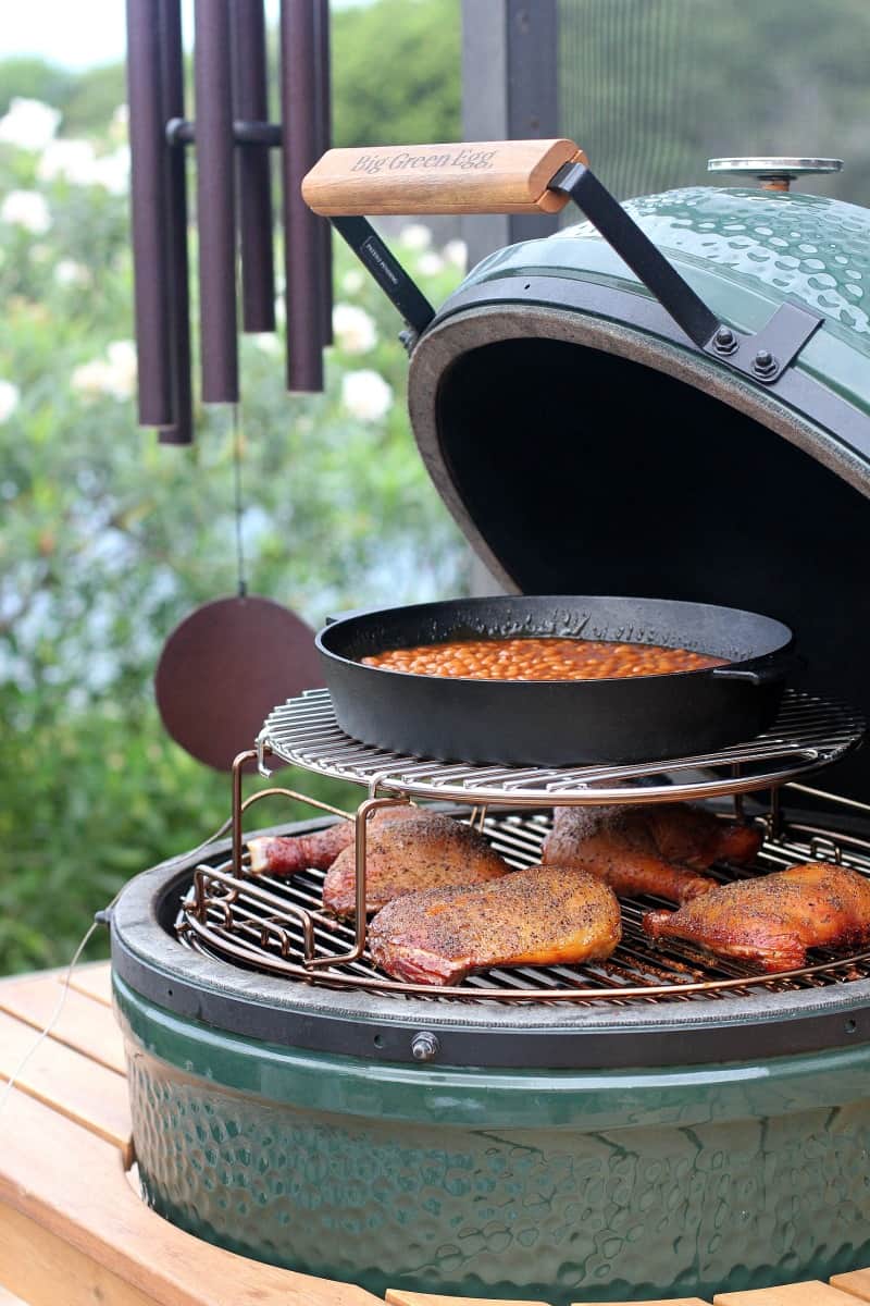 view in a Big Green Egg with chicken cooked on a low grate and a cast iron pan of beans on an upper grate
