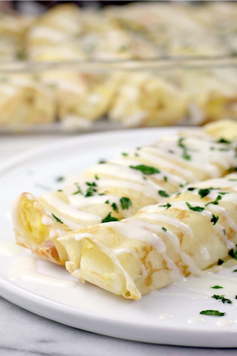 two plated crepes on white dish; casserole dish in background