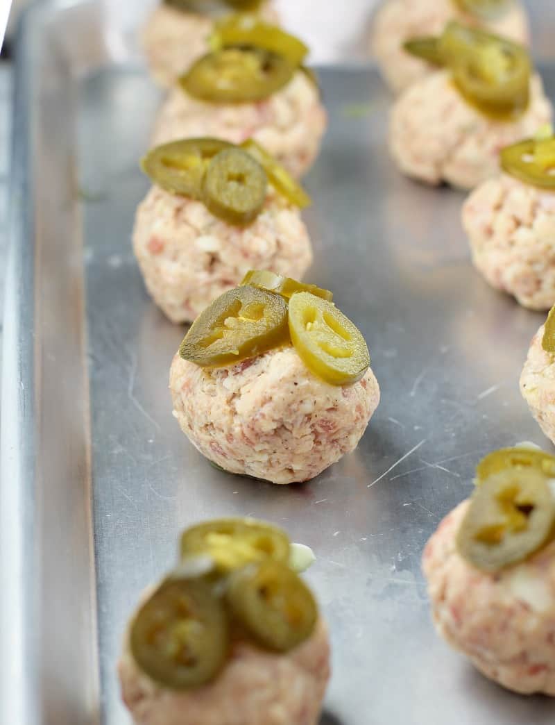 uncooked sausage balls on a bake sheet topped with jalapeno