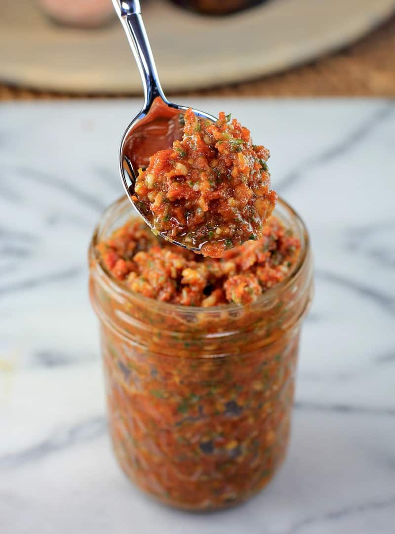 spoon lifting sun dried tomato pesto from a mason jar