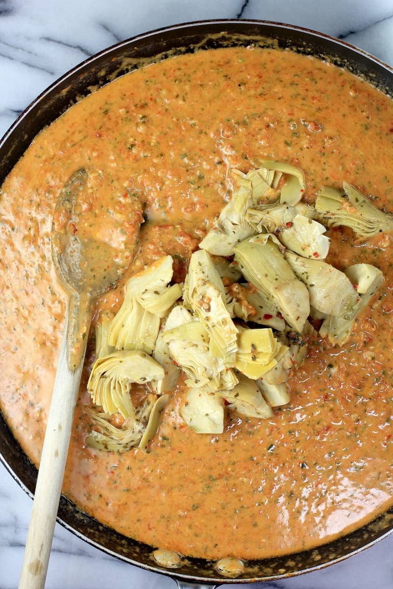 artichoke quarters piled on sun dried tomato pesto sauce in skillet with wooden spoon on the side