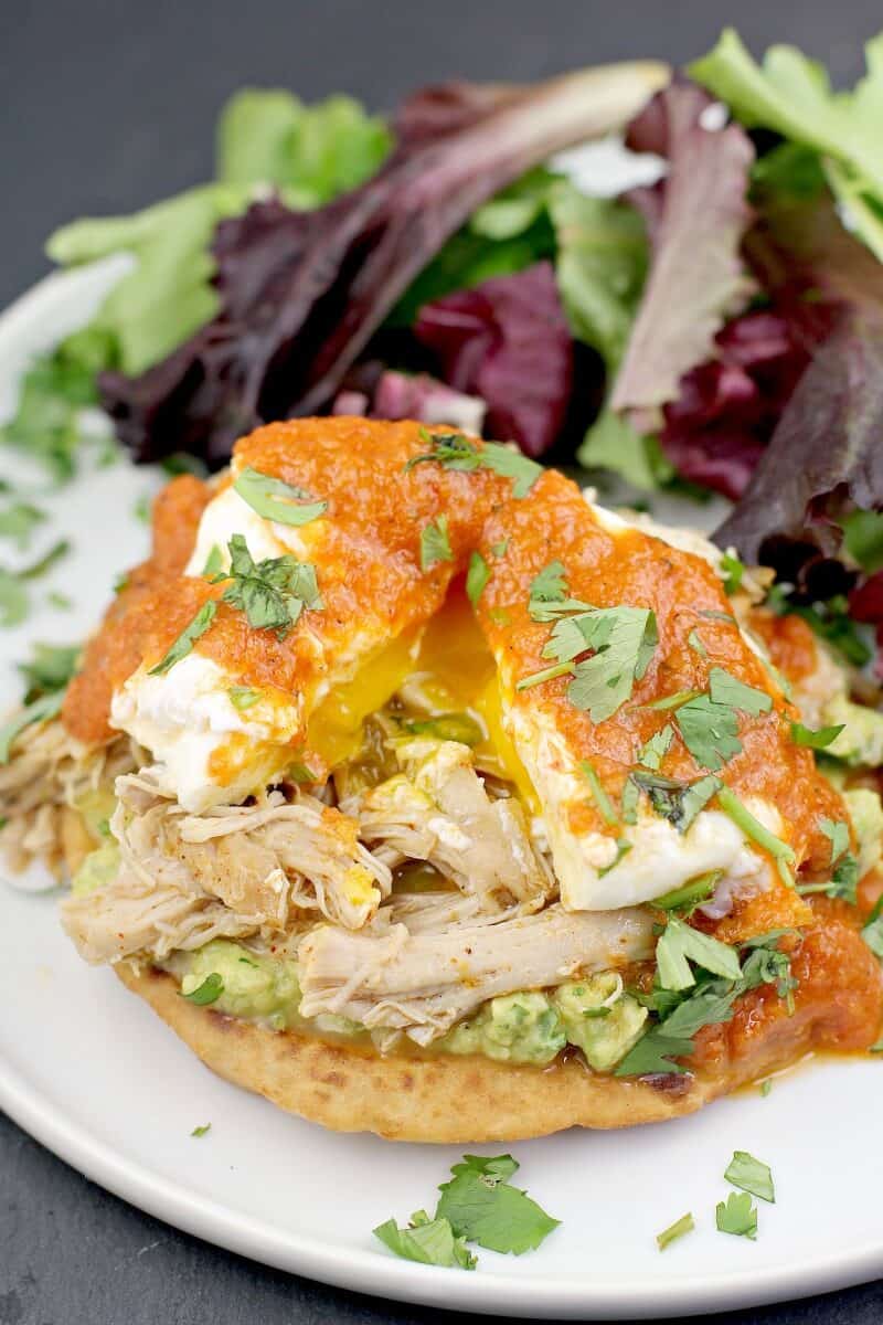 mexican style eggs benedict on a serving plate with side salad; poached egg on top is split to show yolk