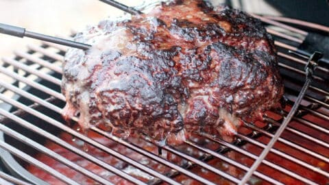 large loaf of smoked ground beef on grill grate in Big Green Egg with temperature probes sticking out