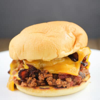 assembled recipe of grilled sloppy joe in a toasted bun with cheddar and bacon; on white plate