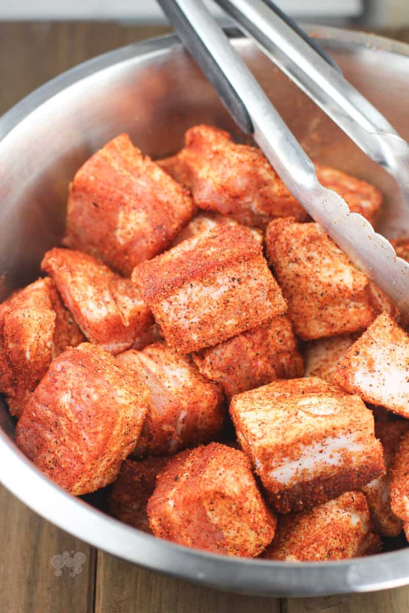 pieces of seasoned pork belly in metal bowl with tongs