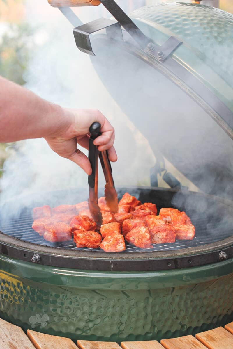 pork belly being placed on grill grate in Big Green Egg