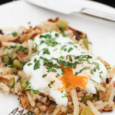 side view of serving of Blackstone griddle hash browns on white plate with egg broken and yolk running out onto potatoes