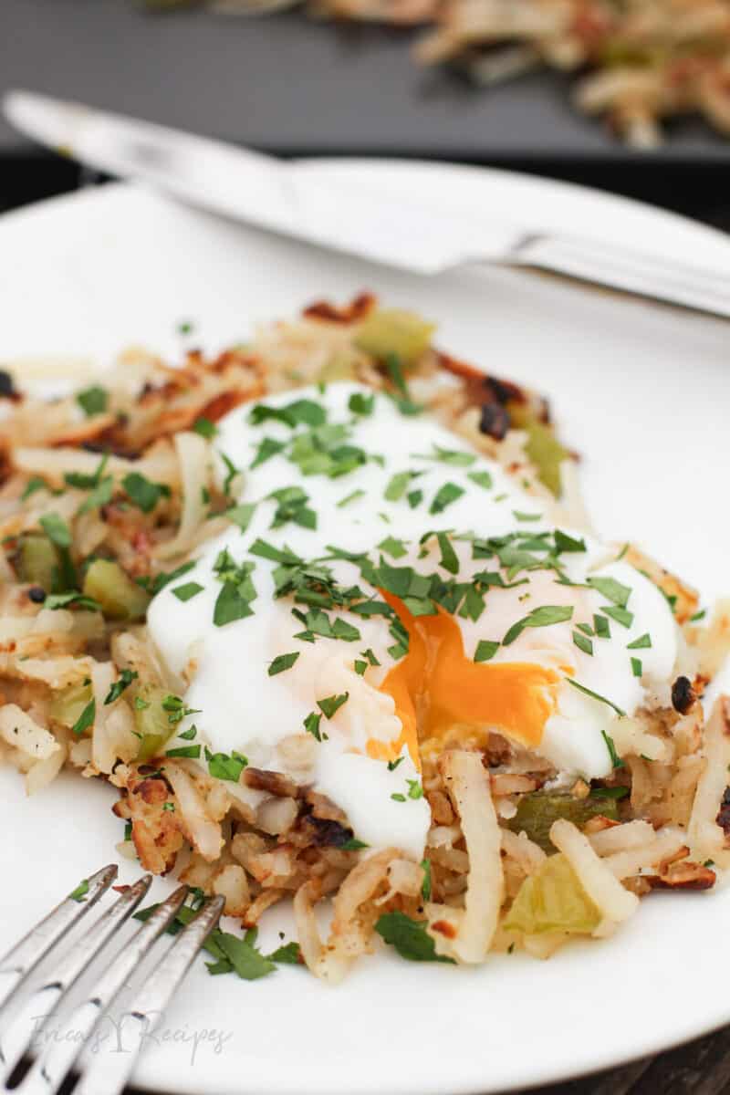 side view of serving of Blackstone griddle hash browns on white plate with egg broken and yolk running out onto potatoes