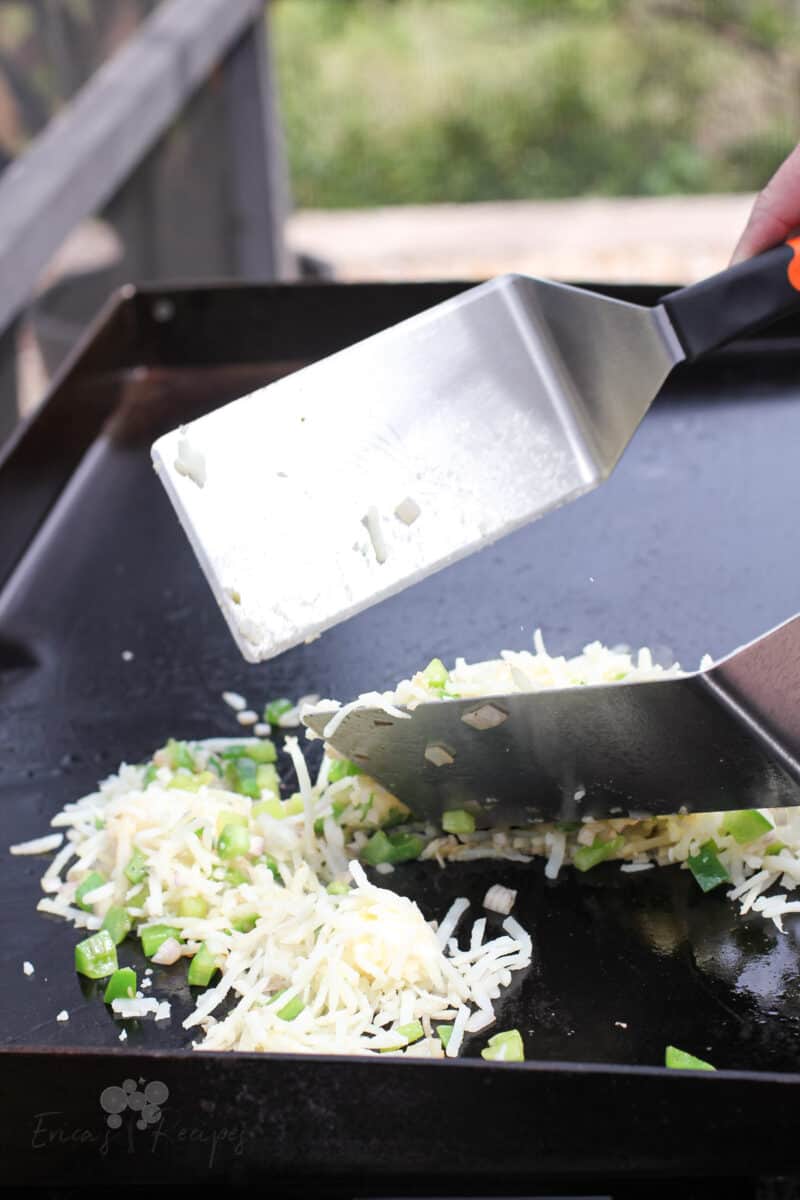 2 spatulas tossing hash browns on Blackstone griddle