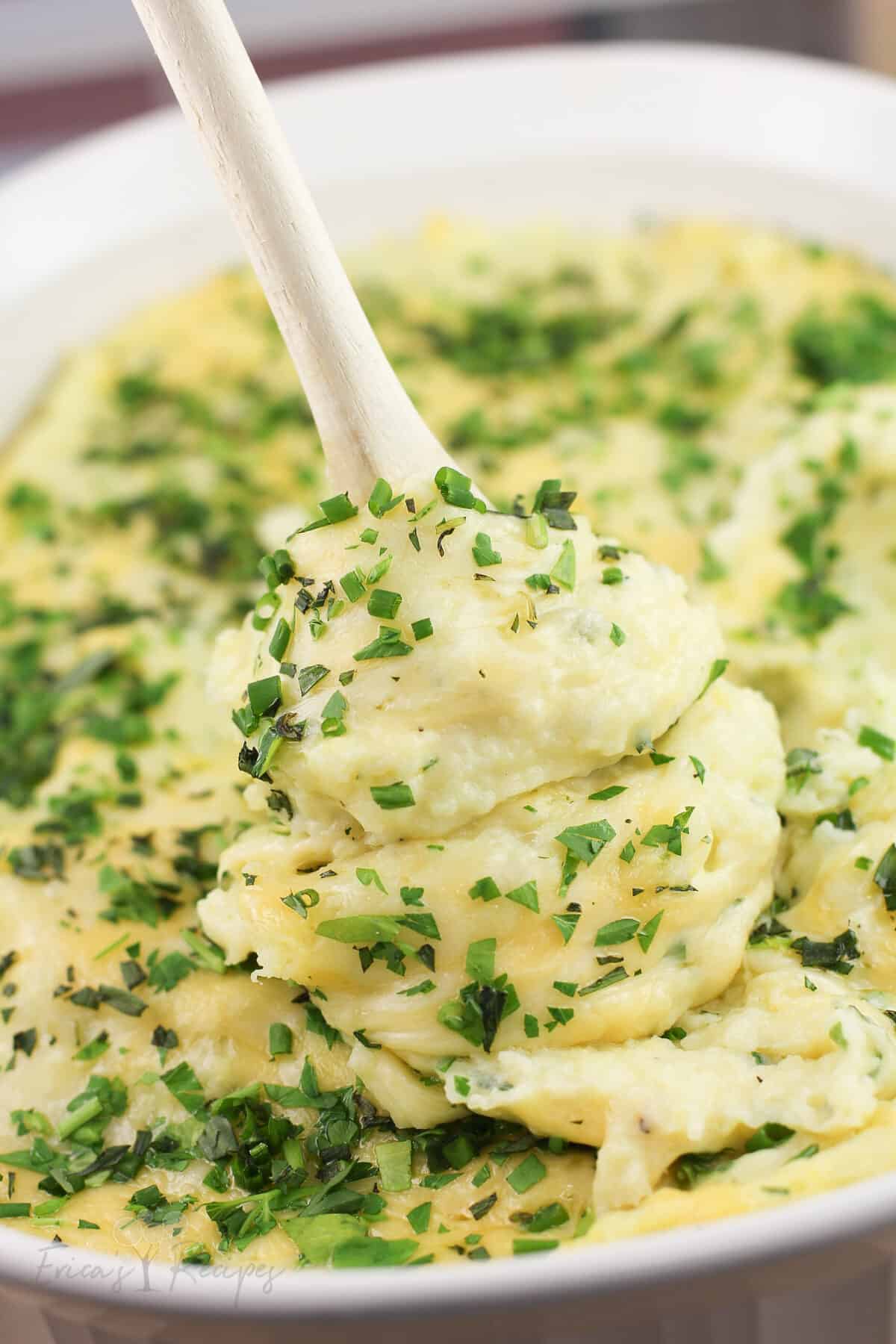 wood spoon lifting up cheesy mashed potatoes from bake dish