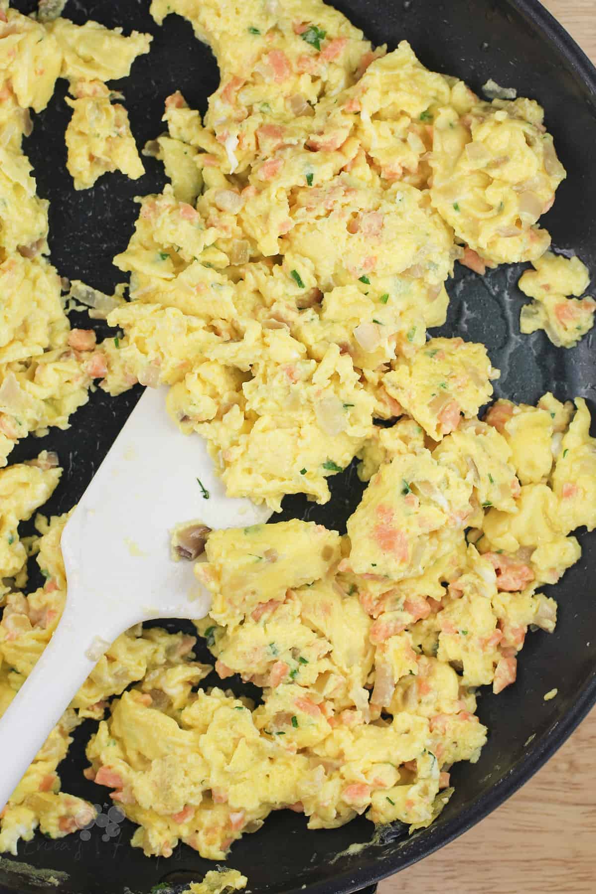 scrambled eggs with smoked salmon in skillet with white rubber spatula