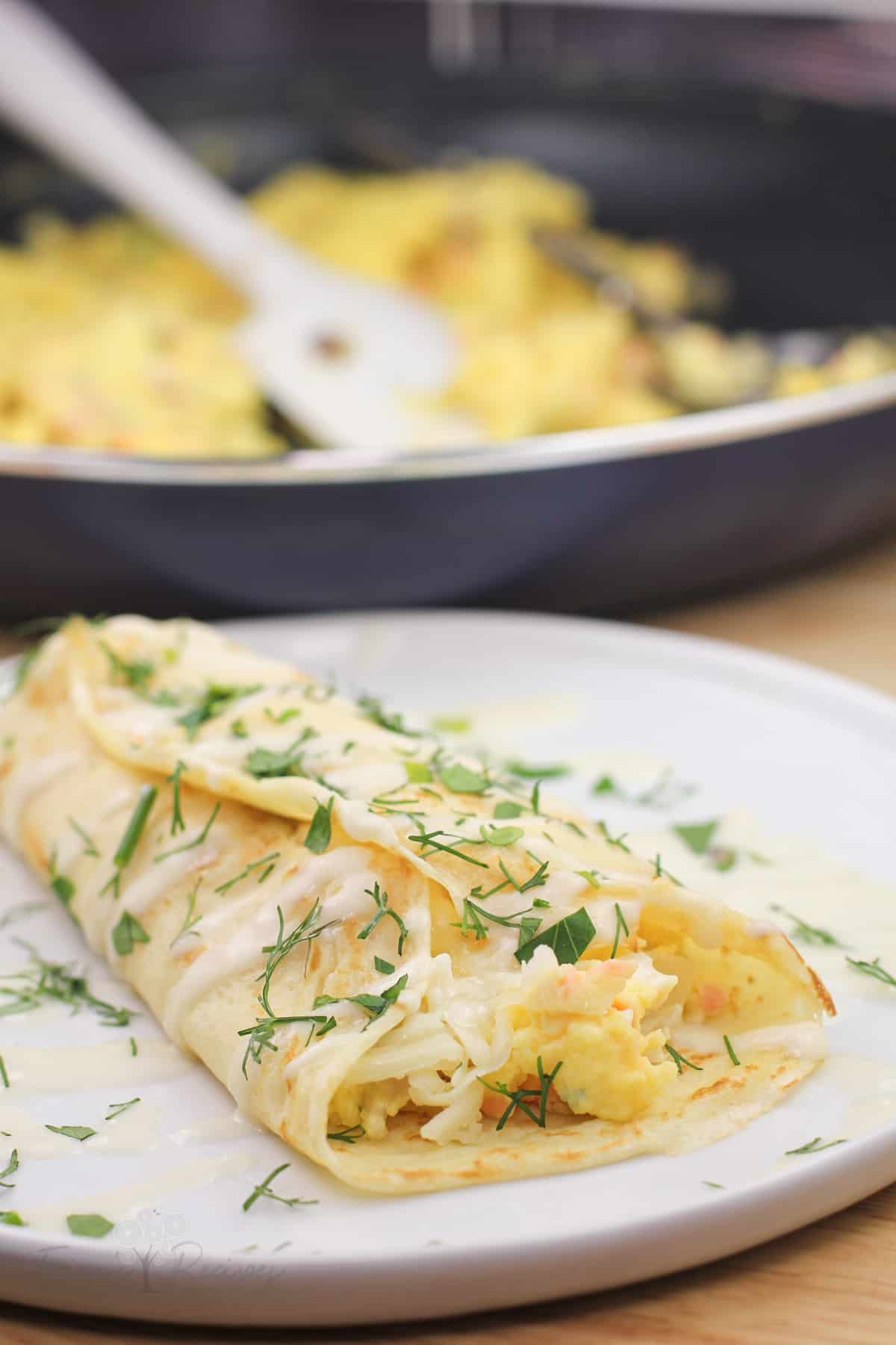 prepared crepe on white plate with skillet in background