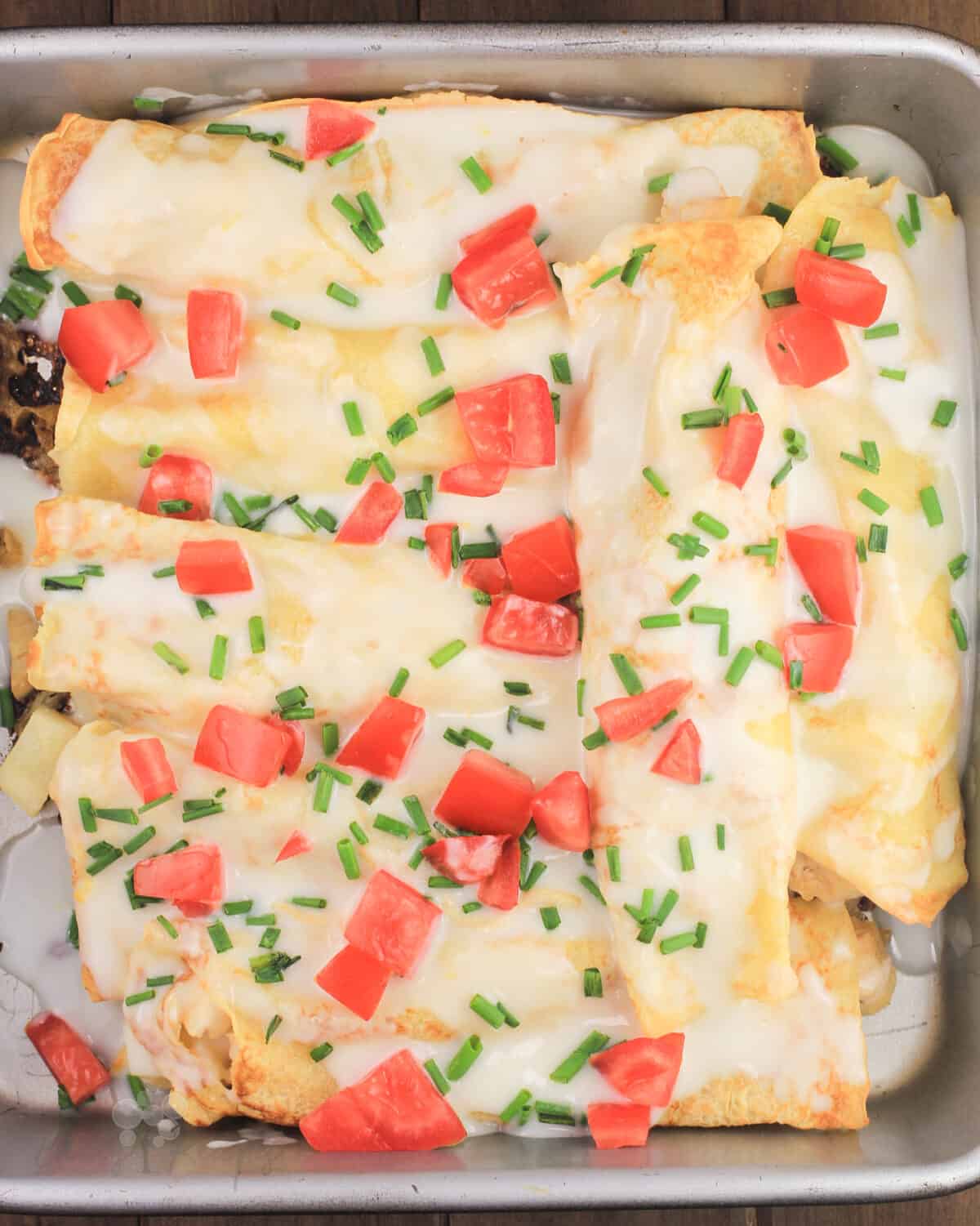 crepes in bake pan covered with lemon bechamel sauce, tomato, and chives