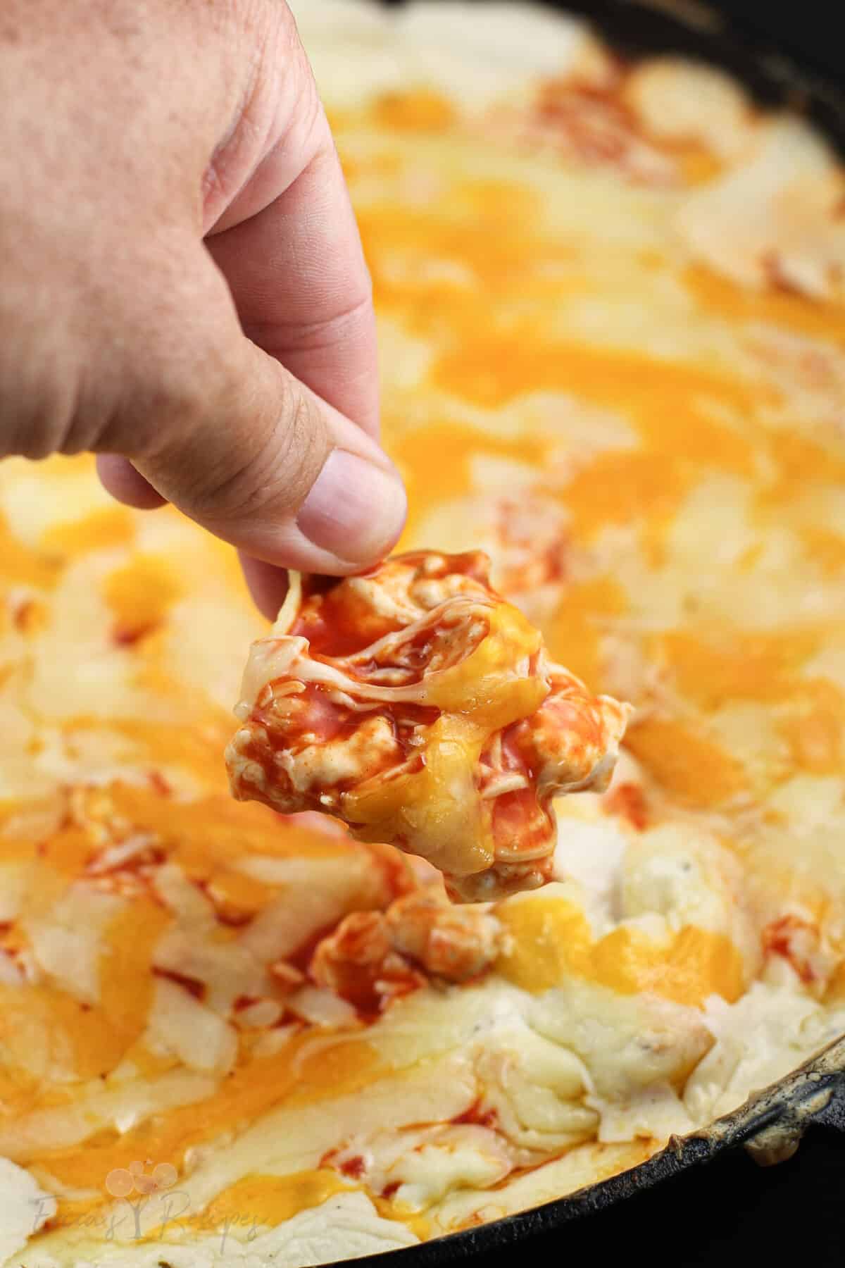 hand holding a tortilla chip to scoop up dip