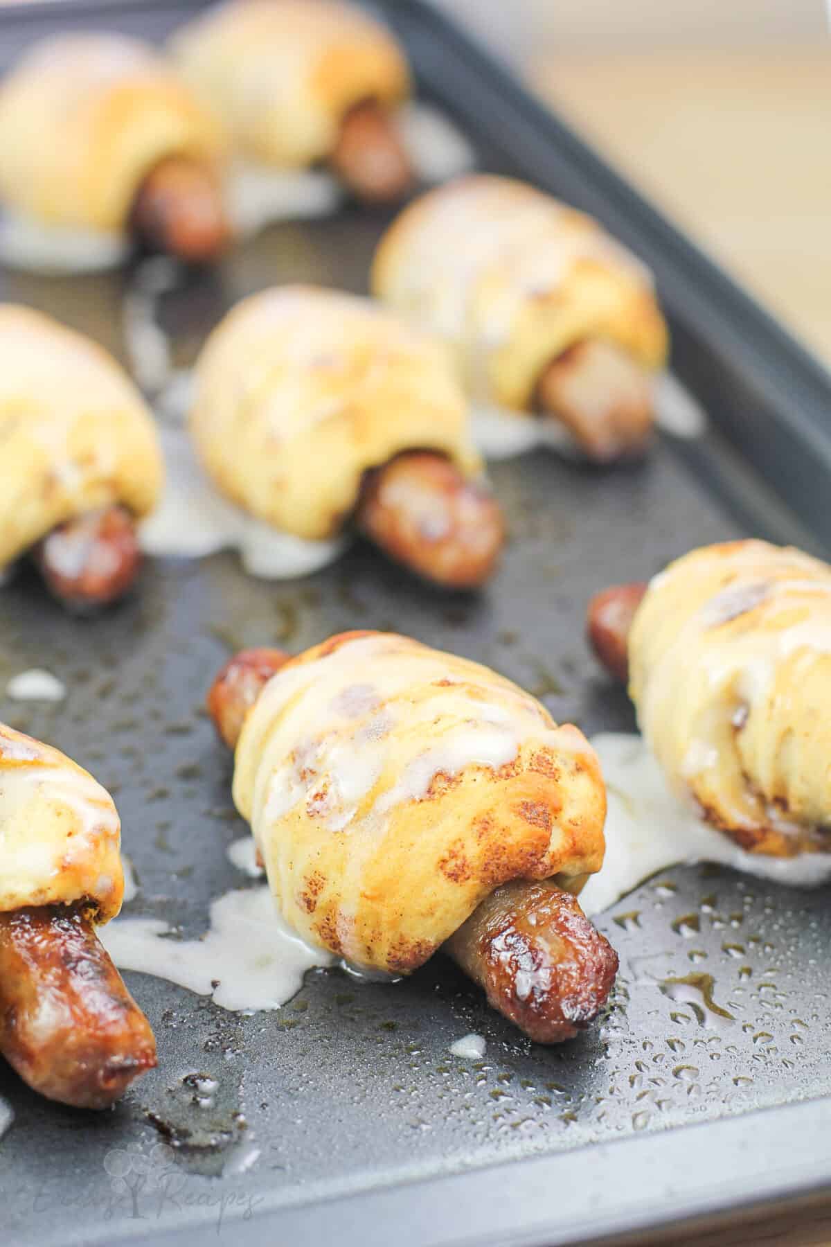 breakfast pigs in a blanket on metal bake sheet topped with icing