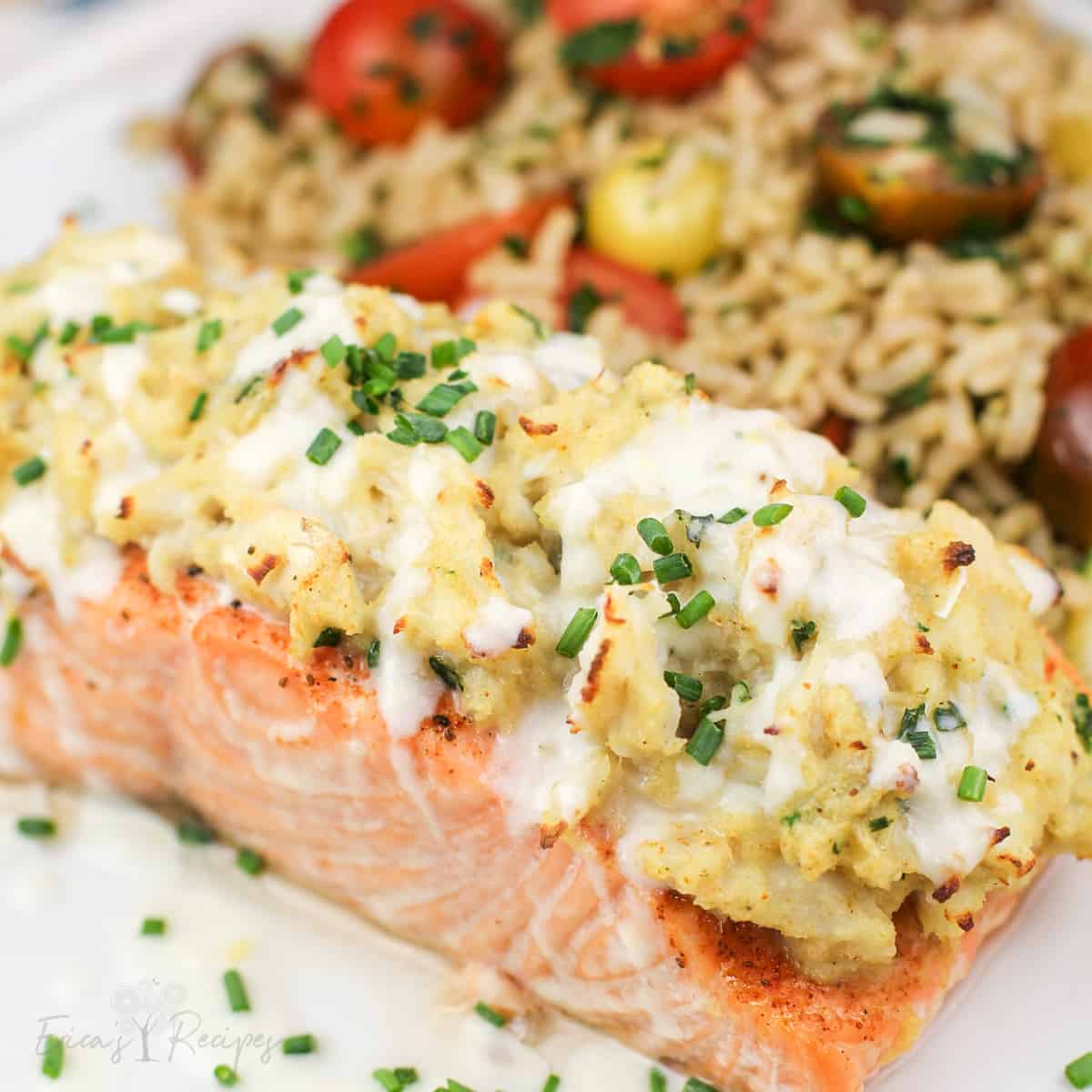 crab stuffed salmon on white plate topped with chives and light lemon sauce. rice with cherry tomatoes in the background