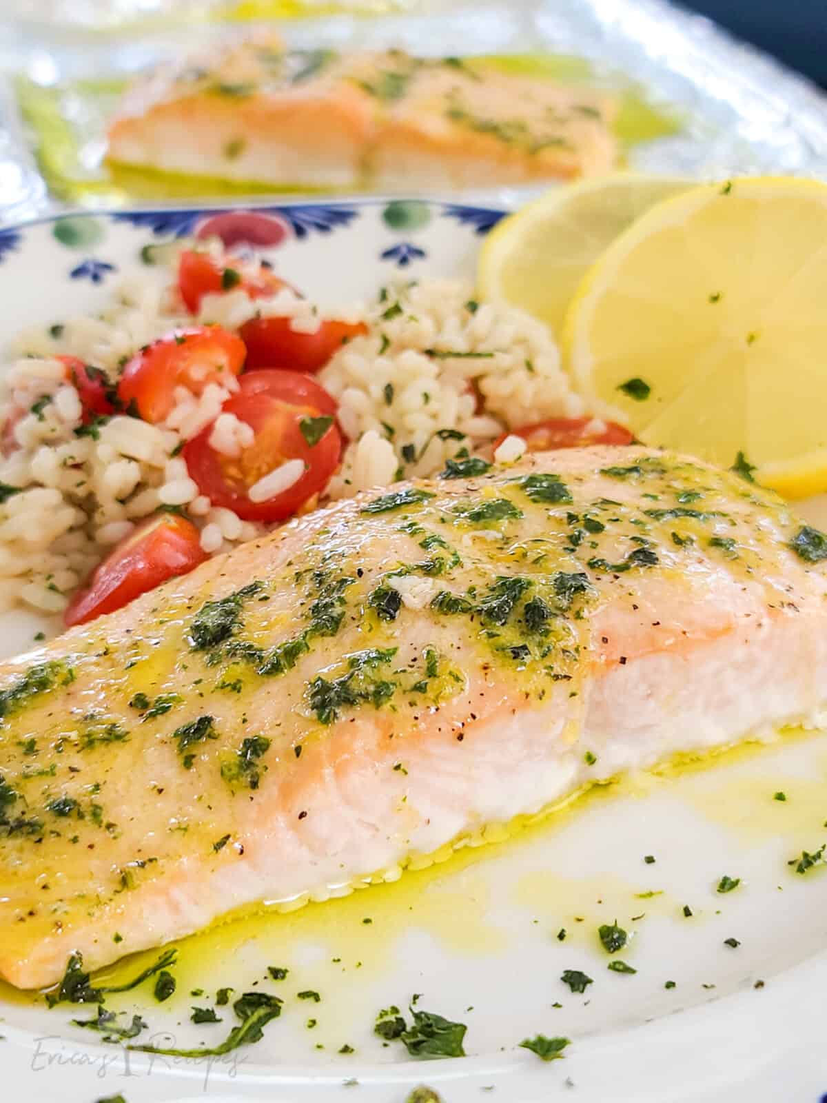 plated salmon topped with lemon basil butter on serving plate with rice and sliced lemon