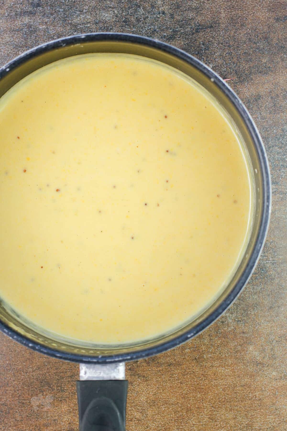 saucepan with beer cheese on brown background