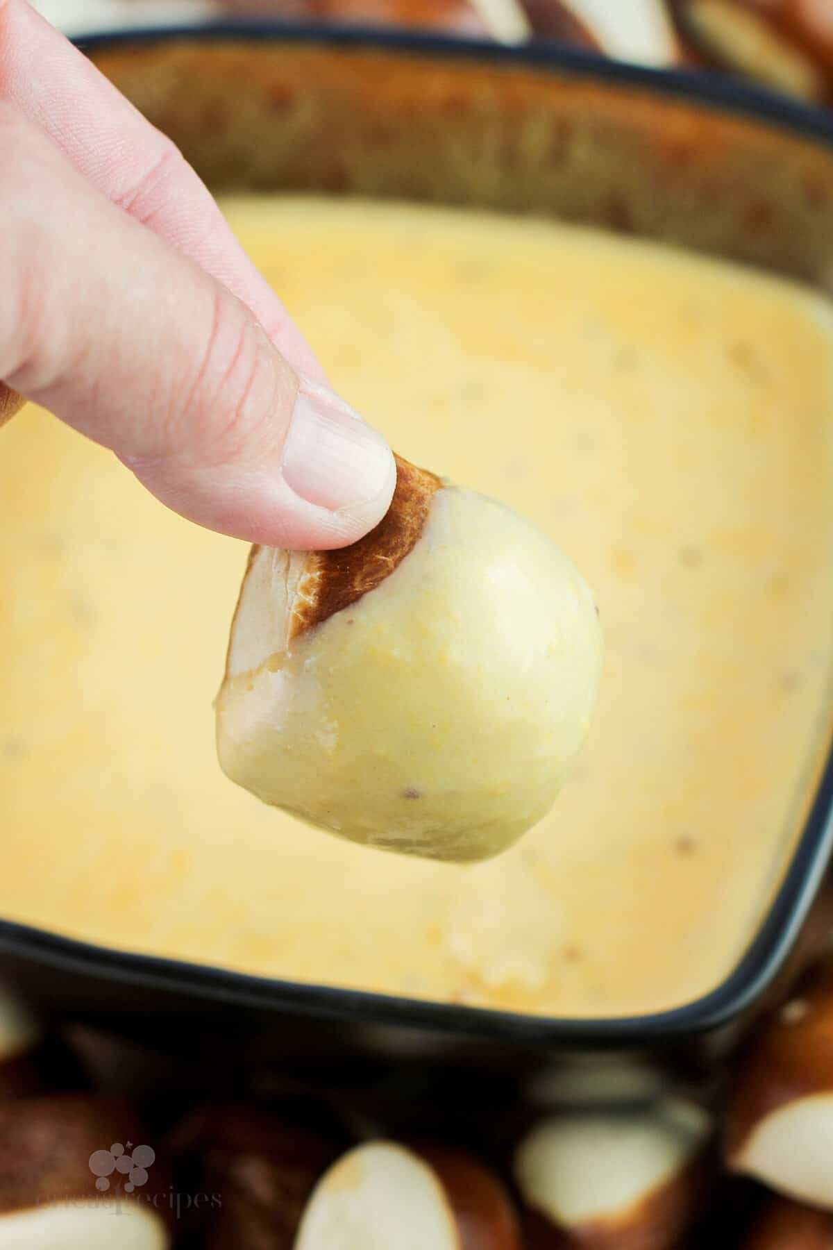 hand holding pretzel bread bite dipped in german cheese dip